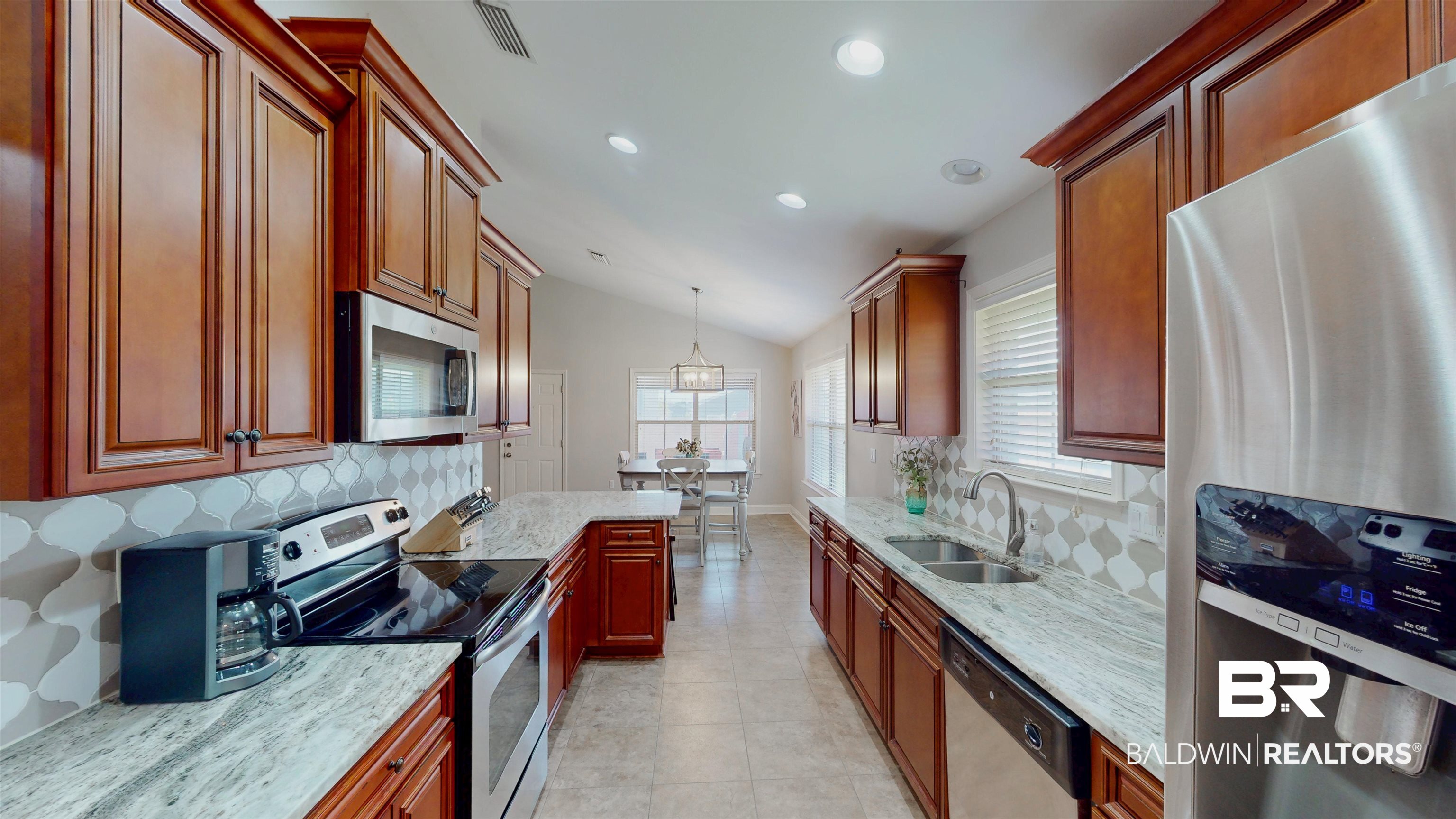 1704 Arcadia Drive Foley, AL 36535 - Photo 14 of 52 Kitchen with appliances with stainless steel finishes, lofted ceiling, decorative backsplash, light stone countertops, and healthy amount of natural light
