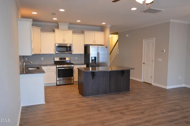 a kitchen with stainless steel appliances granite countertop a stove top oven a sink dishwasher a refrigerator and a dining table with wooden floor