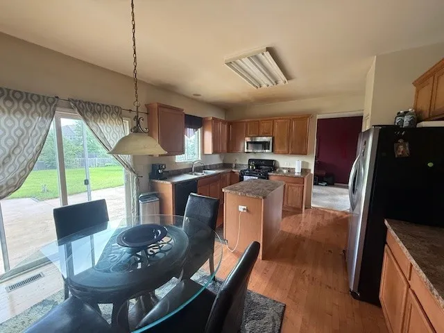 a kitchen with stainless steel appliances granite countertop a refrigerator a stove a sink a dining table and chairs with wooden floor