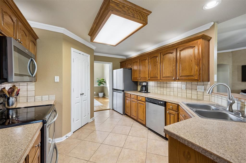 11211 Emerald Ranch Lane Forney, TX 75126 - Photo 19 of 35 Kitchen featuring light wood cabinetry, neutral countertops, stainless steel appliances, tile flooring, and a tile backsplash
