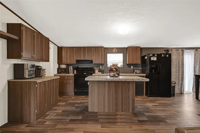 a kitchen with kitchen island granite countertop a refrigerator oven a sink dishwasher and wooden cabinets with wooden floor