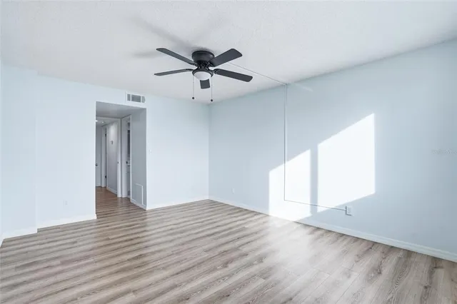 an empty room with wooden floor fan and windows
