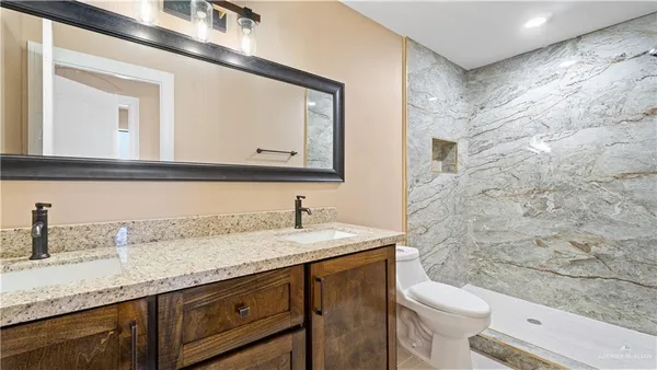 a bathroom with a granite countertop sink vanity mirror and toilet