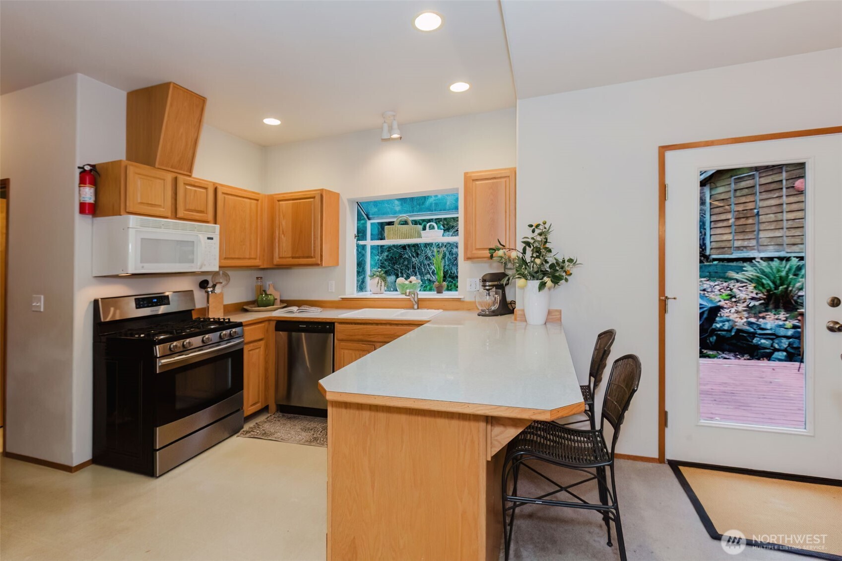 8911 Roanoke Road Northeast Bremerton, WA 98311 - Photo 12 of 40 a kitchen with stainless steel appliances kitchen island a table chairs in it and wooden floors