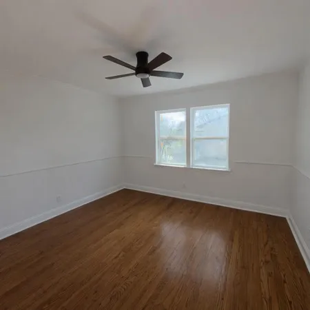 an empty room with wooden floor fan and windows