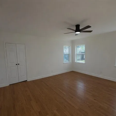an empty room with wooden floor chandelier fan and windows
