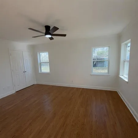 an empty room with wooden floor ceiling fan and windows