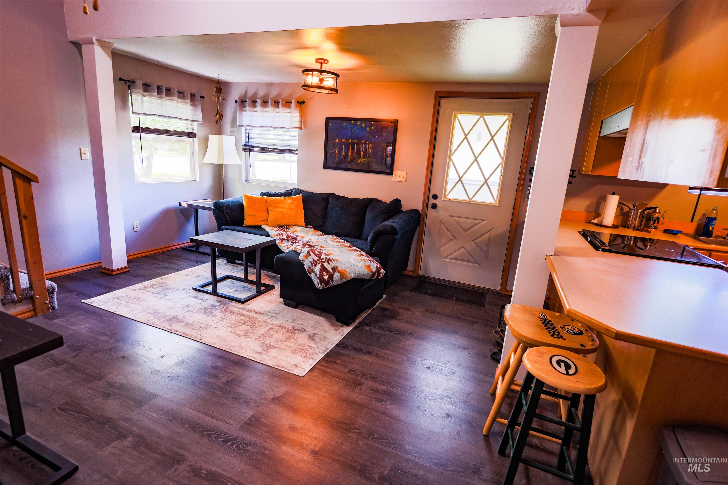 515 8th Street Kamiah, ID 83536 - Photo 15 of 31 Open-concept living area featuring wood-finish flooring, a contemporary ceiling fixture, a white entry door with diamond-pane windows, and a partial view of a kitchen counter with integrated cooktop