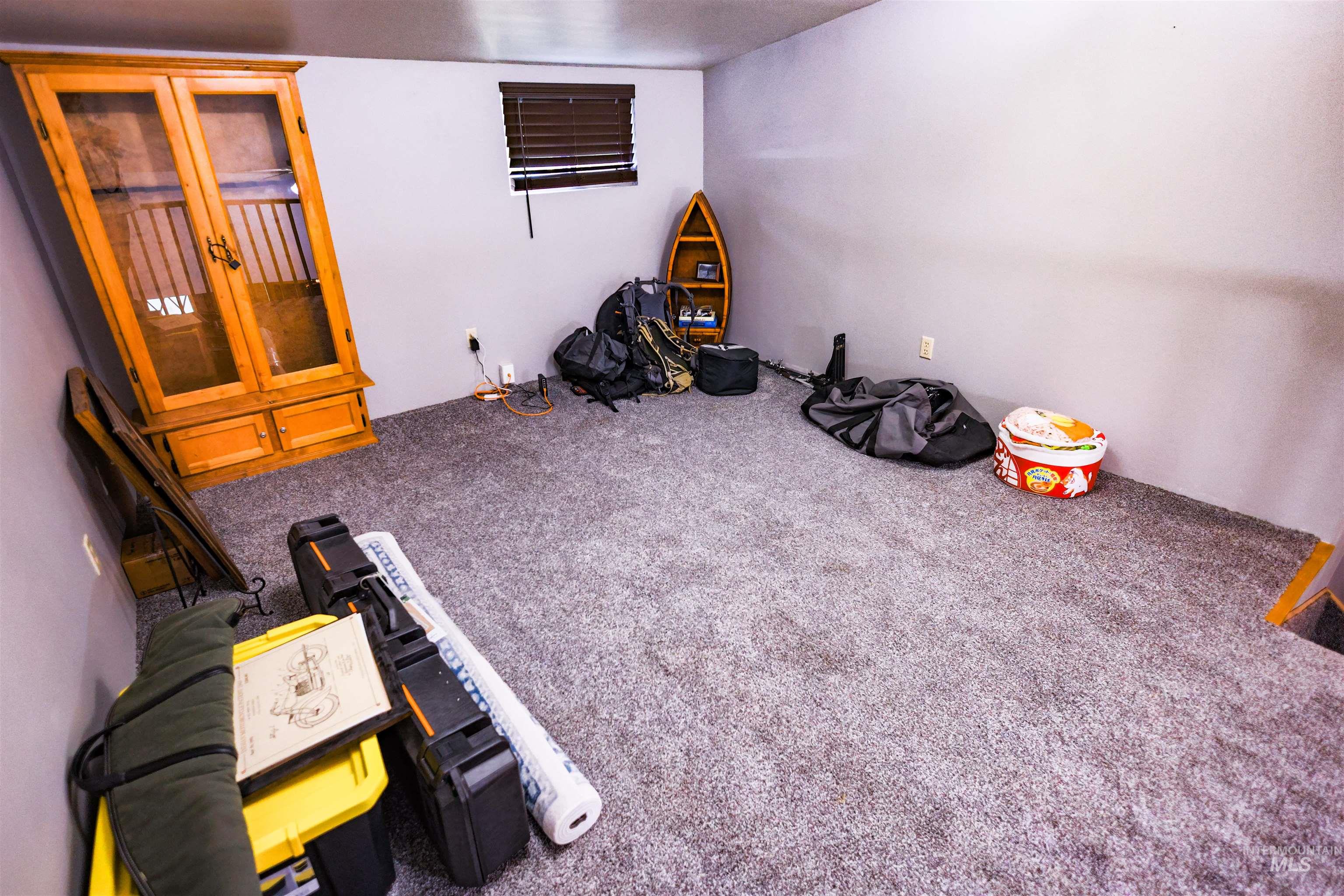 515 8th Street Kamiah, ID 83536 - Photo 21 of 31 Carpeted room featuring a light gray wall finish, a window with brown blinds, and a built-in wooden cabinet with glass doors