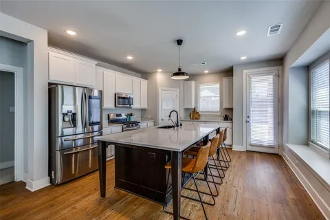 a kitchen with stainless steel appliances granite countertop a refrigerator a sink dishwasher a stove and a refrigerator with wooden floor