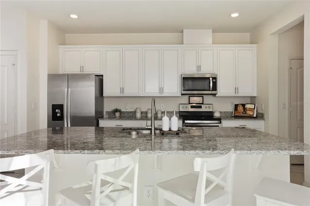 a kitchen with granite countertop a stove a sink a microwave a refrigerator and white cabinets