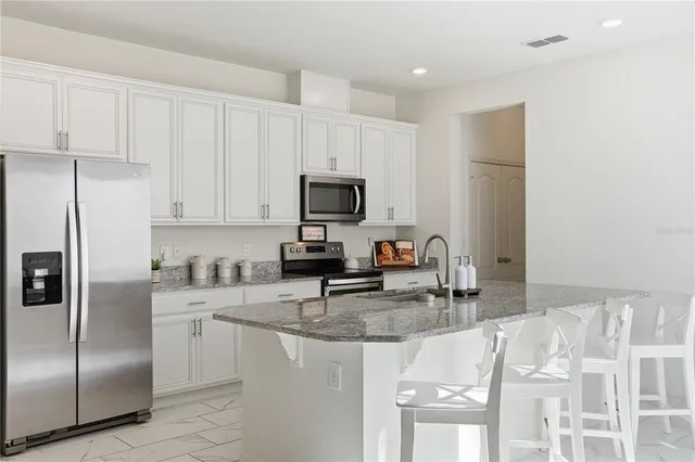 a kitchen with stainless steel appliances granite countertop a sink a stove and a refrigerator with white cabinets