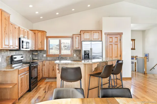 a kitchen with stainless steel appliances granite countertop a stove top oven a sink a dining table and chairs