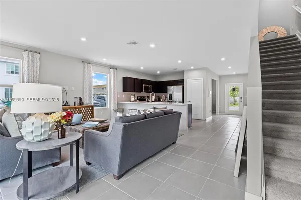 a living room with stainless steel appliances furniture a rug and a kitchen view