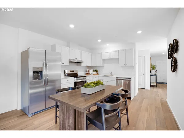 a kitchen with stainless steel appliances kitchen island granite countertop a refrigerator a stove a sink and a dining table with wooden floor