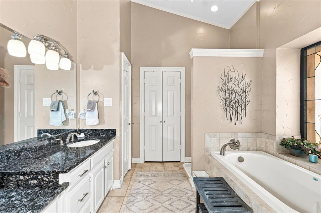 1762 Timber Ridge Circle Corinth, TX 76210 - Photo 20 of 29 Double vanity with dark stone countertop, built-in bathtub with tiled surround, and vaulted ceiling