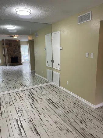 a view of an empty room with wooden floor and a kitchen