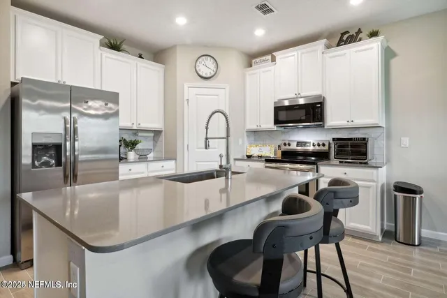 a kitchen with stainless steel appliances granite countertop a sink a stove a refrigerator cabinets and a dining table with wooden floor