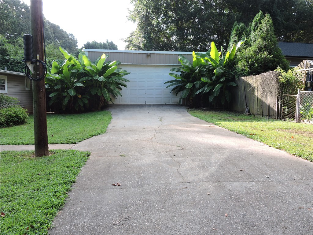 1901 Hattons Ford Road Townville, SC 29689 - Photo 5 of 33 A lengthy concrete driveway leads to a garage entrance, flanked by mature landscaping and a wooden privacy fence.
