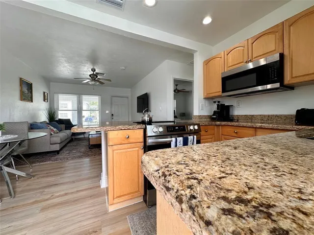 a kitchen with stainless steel appliances granite countertop a stove top oven a sink dishwasher a dining table and chairs with wooden floor