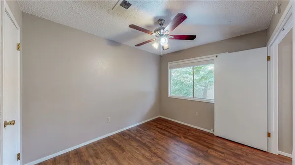 an empty room with wooden floor fan and windows