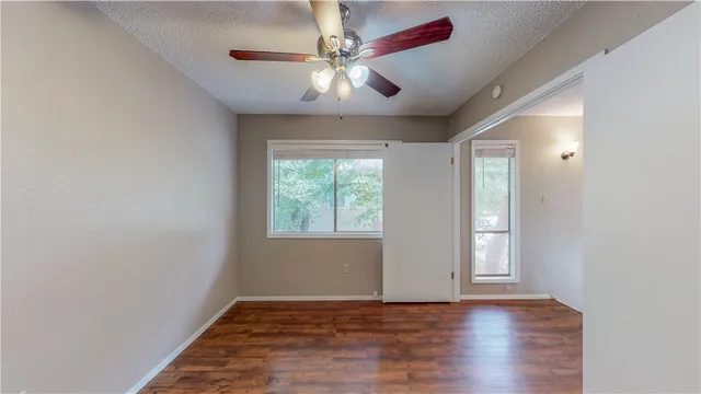 an empty room with wooden floor chandelier fan and windows