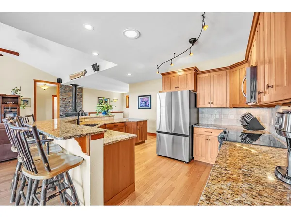 a kitchen with stainless steel appliances kitchen island granite countertop a refrigerator a stove top oven and a dining table with wooden floor