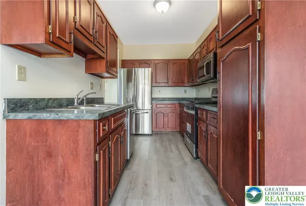 a kitchen with stainless steel appliances granite countertop a refrigerator a sink dishwasher a stove and white countertops with wooden floor