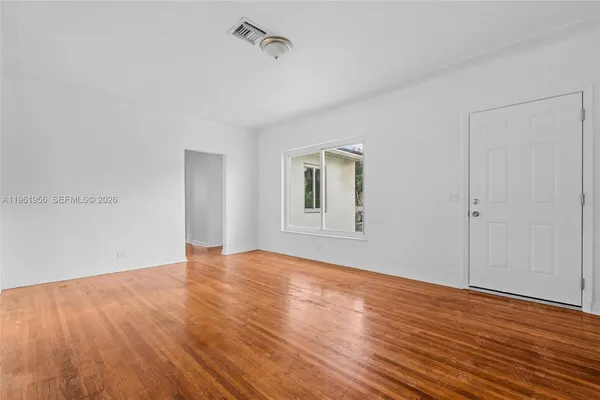 a view of an empty room with wooden floor and a window
