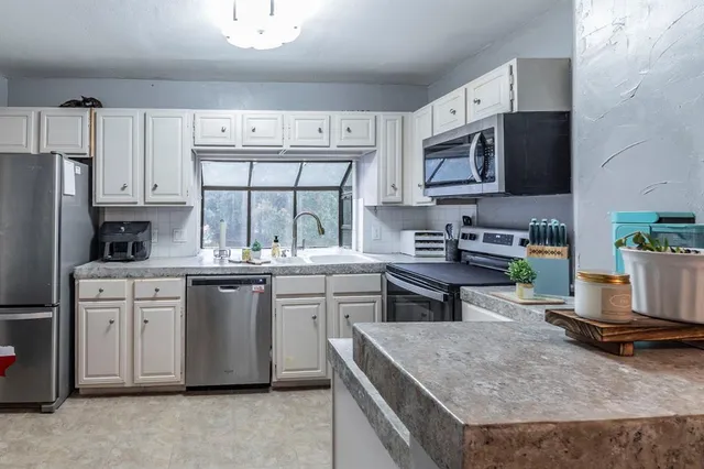 a kitchen with stainless steel appliances granite countertop a stove a sink dishwasher and a microwave oven with white cabinets