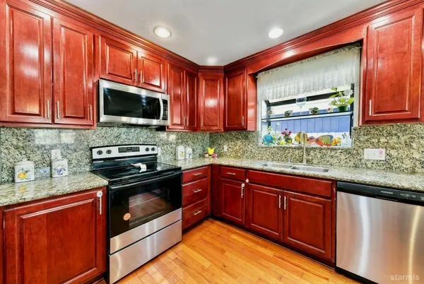 a kitchen with stainless steel appliances granite countertop wooden cabinets a stove top oven a granite counter and a wooden floors