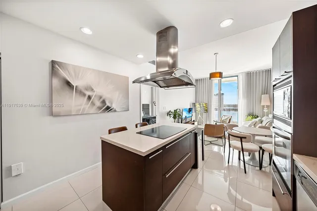 a kitchen with stainless steel appliances a sink a stove a refrigerator a dining table and chairs with wooden floor