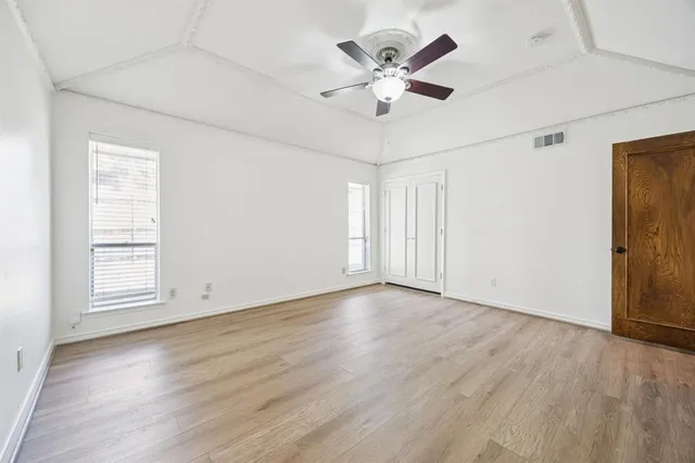 an empty room with wooden floor chandelier fan and windows