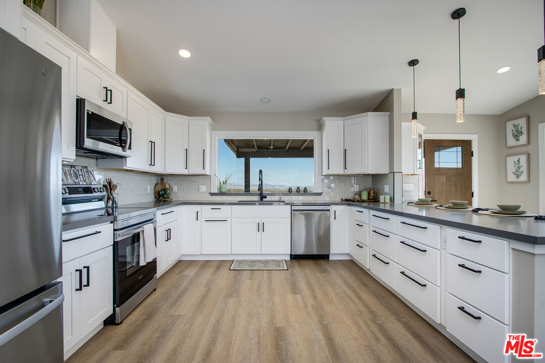 60777 Adele Road Landers, CA 92285 - Photo 13 of 43 a large kitchen with granite countertop a stove top oven a sink dishwasher and white cabinets with wooden floor