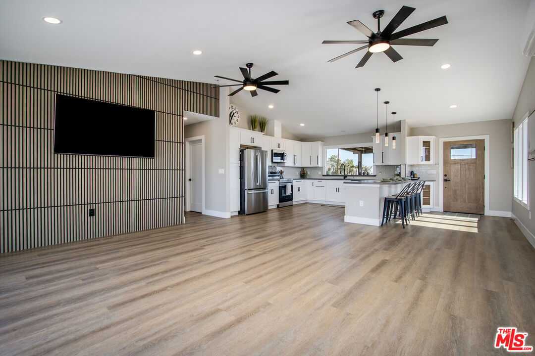 60777 Adele Road Landers, CA 92285 - Photo 7 of 43 a view of a kitchen with a flat screen tv a wooden floor and a ceiling fan