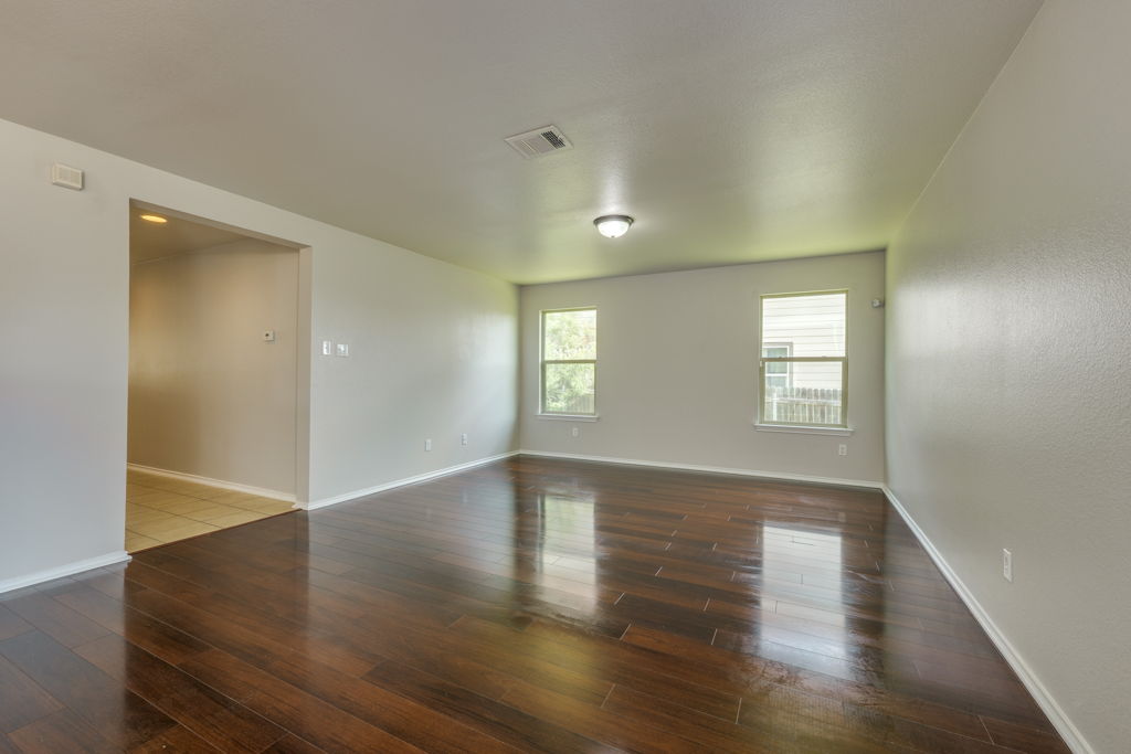 210 Cushman Drive Kyle, TX 78640 - Photo 4 of 21 Spacious room featuring wood-finish flooring, light neutral wall paint, two windows, and a ceiling-mounted light fixture