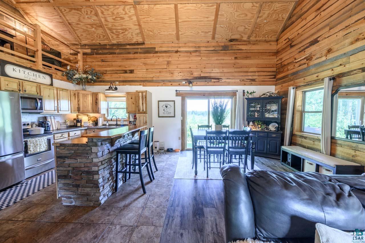 Open-concept living space featuring exposed wood beam ceilings, wood-finish flooring throughout, and a central kitchen island with brick detailing