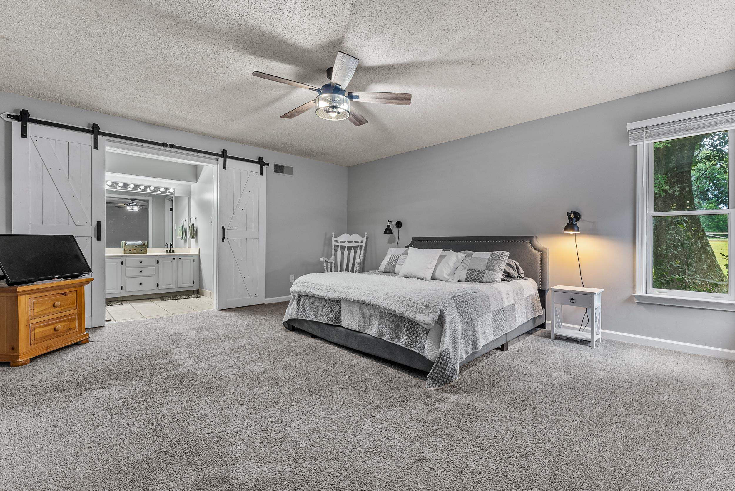 12389 Macon Road Collierville, TN 38017 - Photo 23 of 37 Bedroom featuring a textured ceiling, ceiling fan, ensuite bathroom, a barn door, and light carpet
