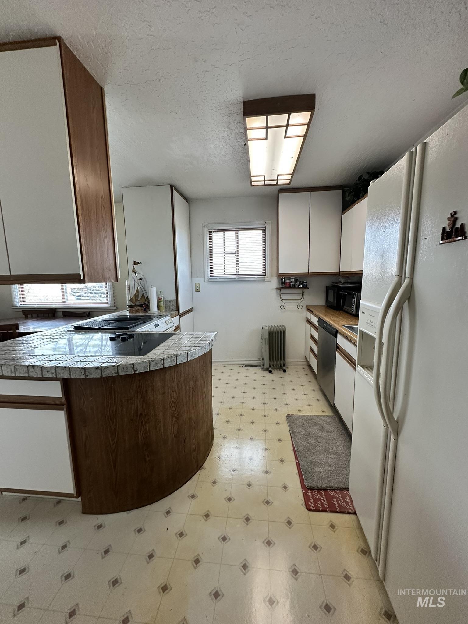 6750 Dearborne Road Nampa, ID 83686 - Photo 11 of 26 Dual tone kitchen featuring light flooring, white fridge with ice dispenser, a textured ceiling, tile countertops, and radiator