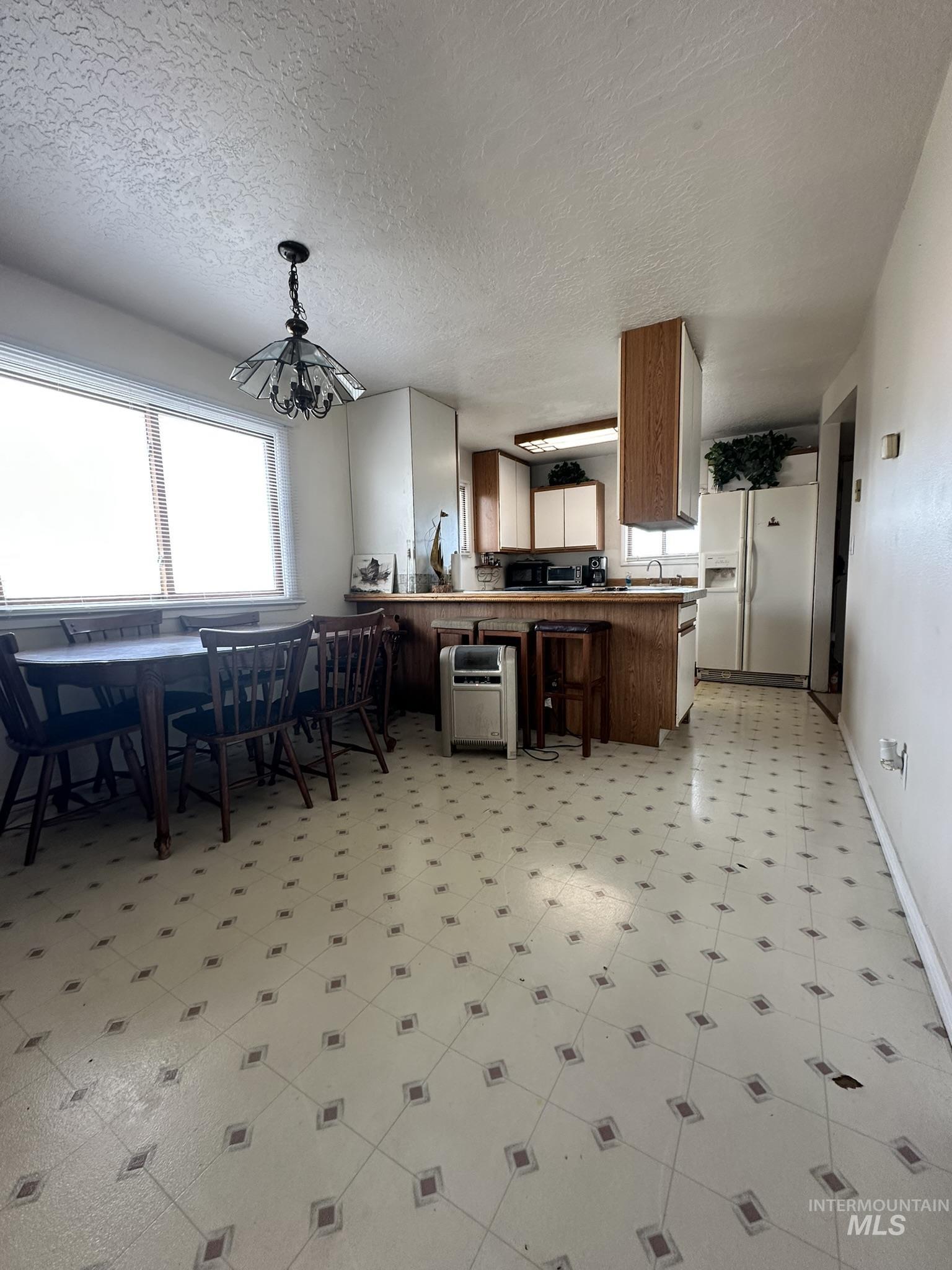 6750 Dearborne Road Nampa, ID 83686 - Photo 10 of 26 Kitchen featuring light floors, a peninsula, white fridge with ice dispenser, wood finish cabinets, and hanging lights