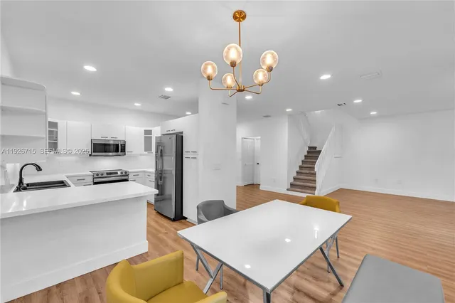 a kitchen with stainless steel appliances granite countertop a sink a stove a refrigerator and a dining table with wooden floor