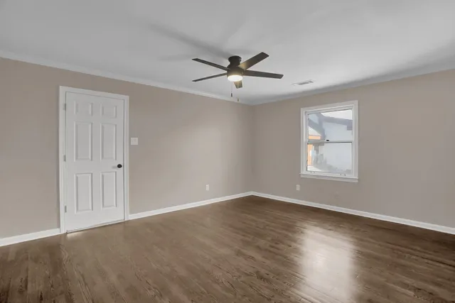 an empty room with wooden floor ceiling fan and windows