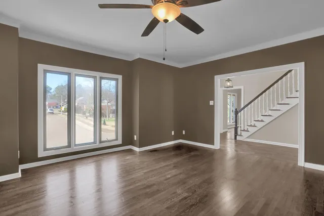 a view of an empty room with wooden floor and fan