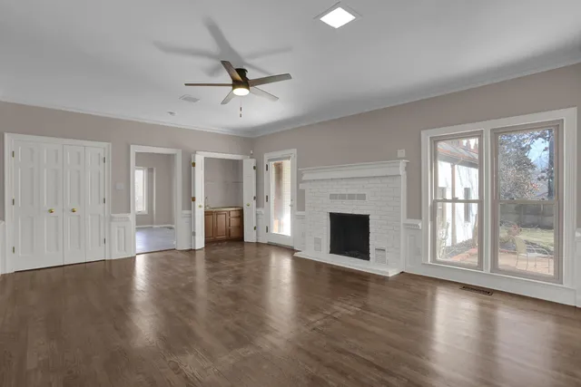 an empty room with wooden floor fireplace and windows