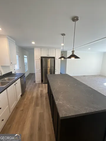 a open kitchen with stainless steel appliances granite countertop a sink dishwasher a refrigerator and white cabinets with wooden floor