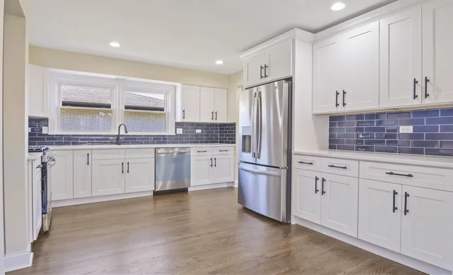 a kitchen with stainless steel appliances white cabinets a sink a stove a microwave and wooden floors