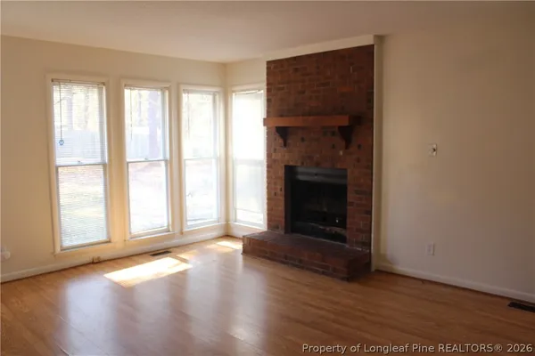 an empty room with wooden floor fireplace and windows