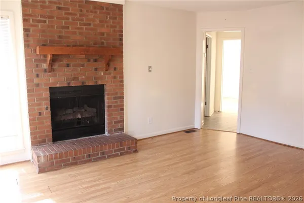 a view of an empty room with wooden floor and a fireplace