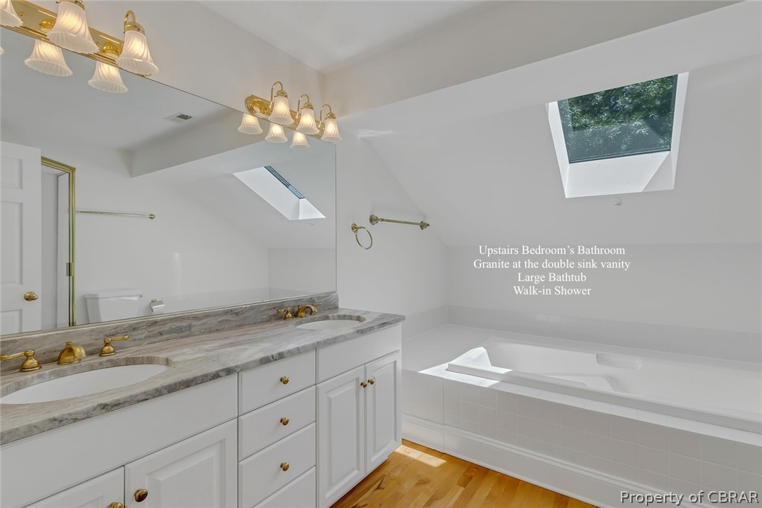 5818 Rivers Landing Terrace, Unit 5818 White Stone, VA 22578 - Photo 32 of 50 Bathroom with vanity with extensive cabinet space, lofted ceiling with skylight, tiled tub, hardwood / wood-style flooring, and dual sinks