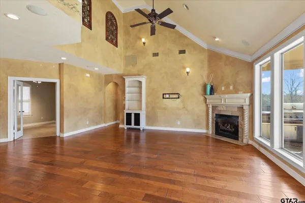 an empty room with wooden floor a fireplace a ceiling fan and windows